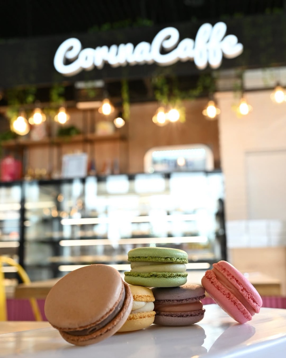 Macarons colorați pe masa din cofetărie, cu vitrina și firma luminoasă în spate